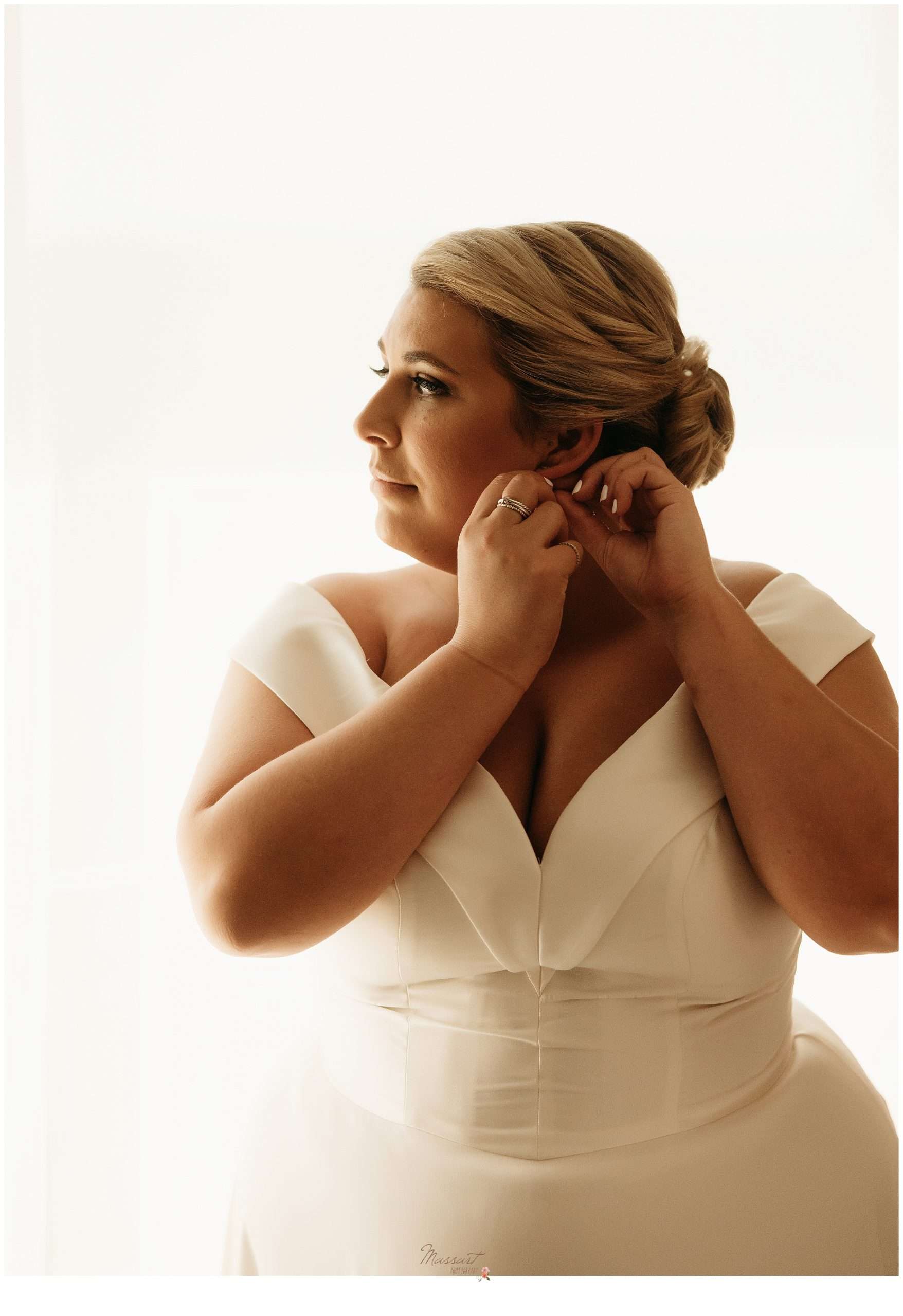 bride adjusts earrings standing in wedding gown for Rhode Island wedding day