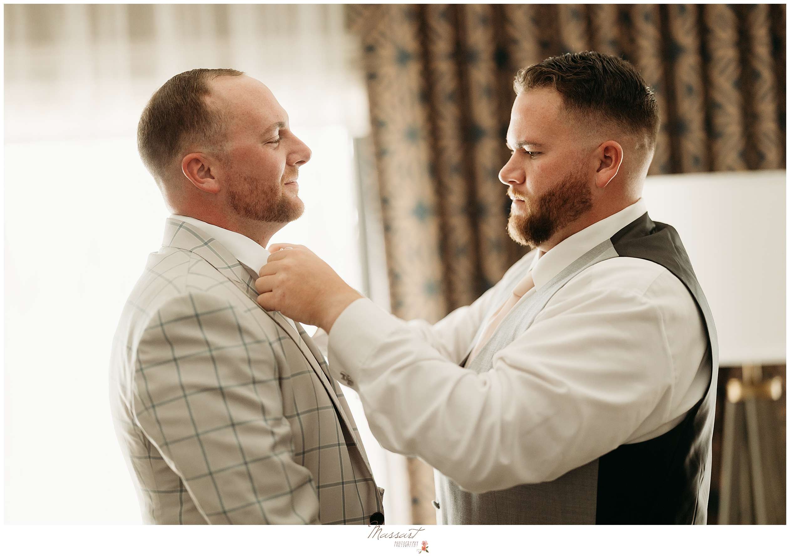 groomsman adjusts groom's tie during prep at Rhode Island hotel room