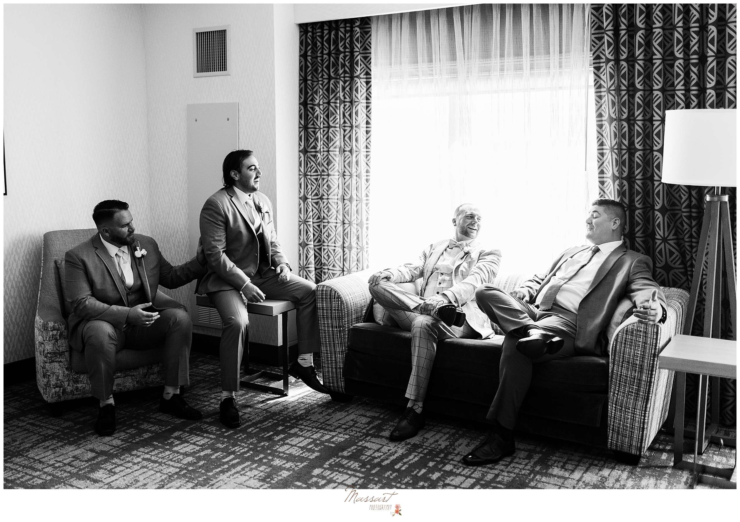 groom sits talking with groomsmen in hotel room before RI wedding day