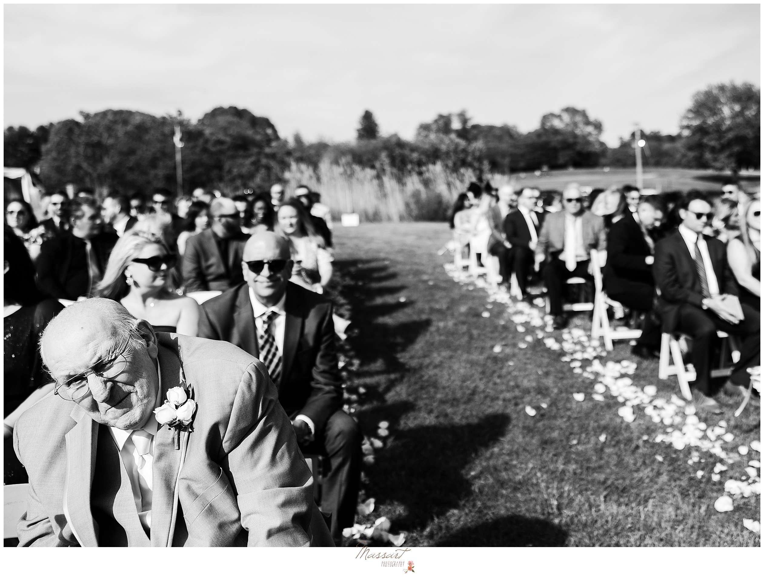 wedding guests sit on lawn by aisle lined by flower petals at Harbor Lights