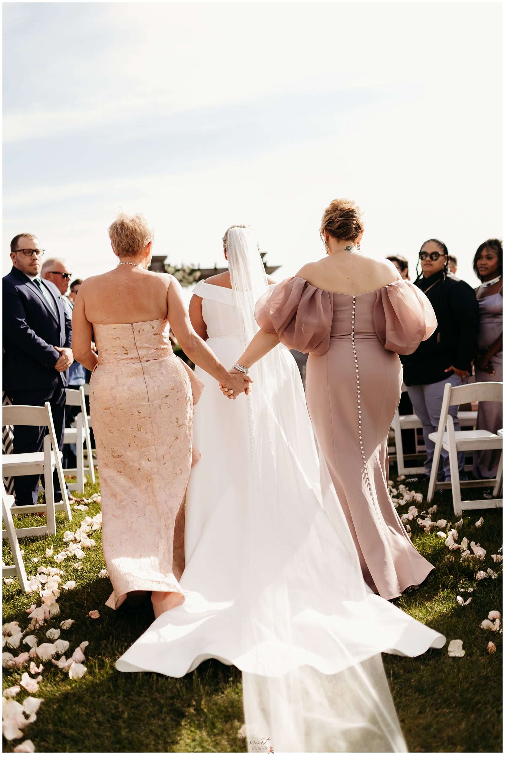 women hold hands walking behind bride down aisle at Harbor Lights